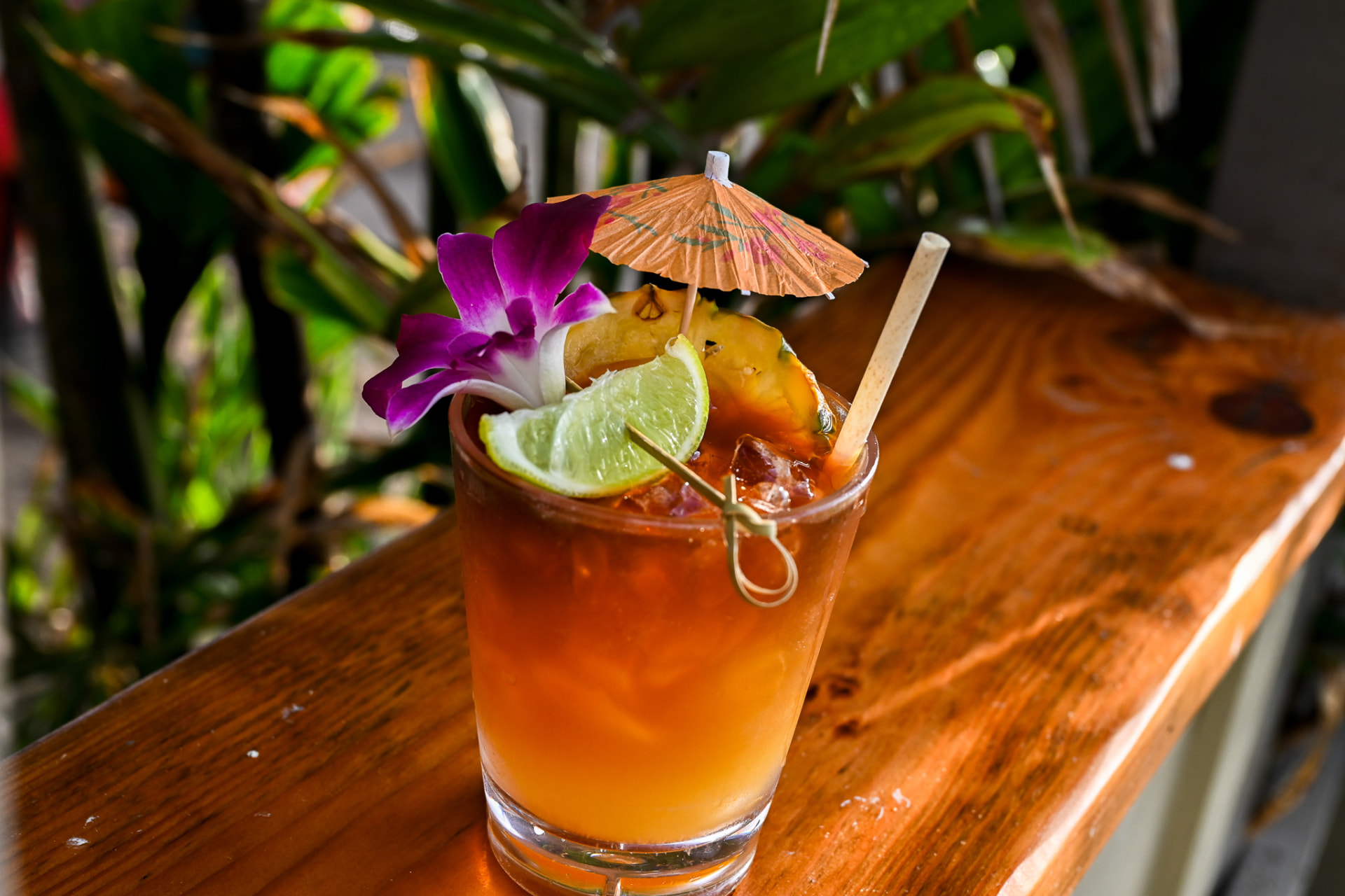 Mai tai with orchid and pineapple on a wooden rail