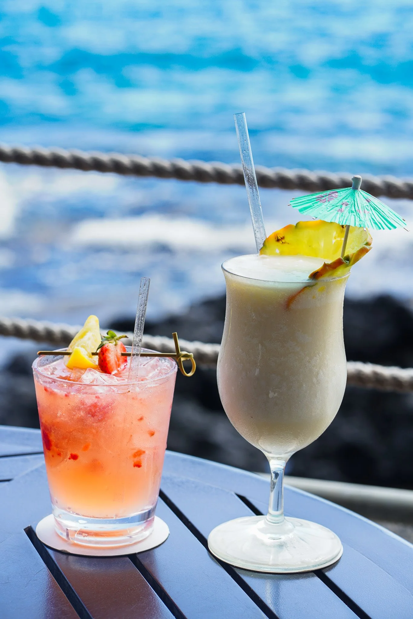 Strawberry cocktail and frozen piña colada on the rail above the surf