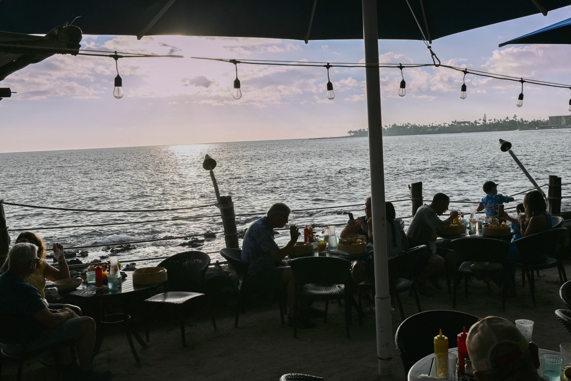 Guests dining on the sand as the sun sets over the water