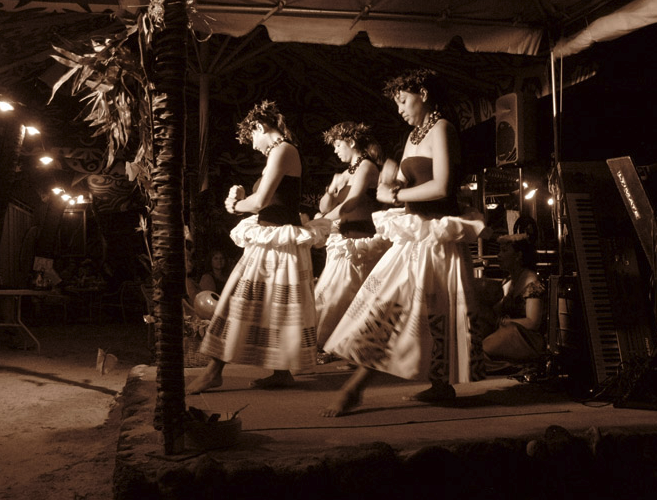 Three hula dancers in traditional skirts performing on stage at night