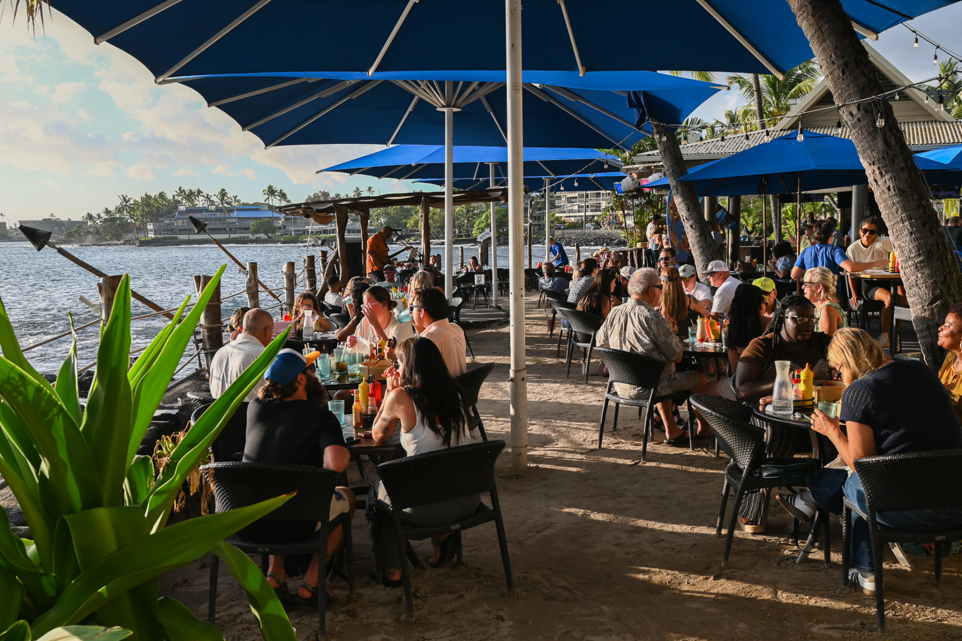 Oceanfront tables under blue umbrellas at golden hour